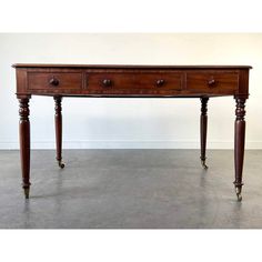 an antique wooden table with three drawers on one side and two turned down legs at the bottom