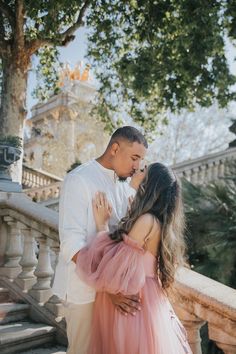 a man and woman standing next to each other in front of some stairs with trees