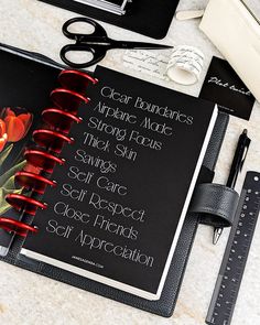 an open notebook with writing on it next to some scissors and other items that include pens