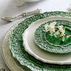 a green and white place setting with flowers on the plate, silverware and utensils