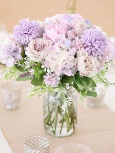 a vase filled with purple and white flowers on top of a table next to glasses