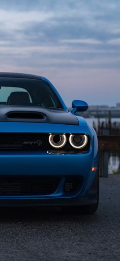 the front end of a blue sports car parked near a body of water at dusk