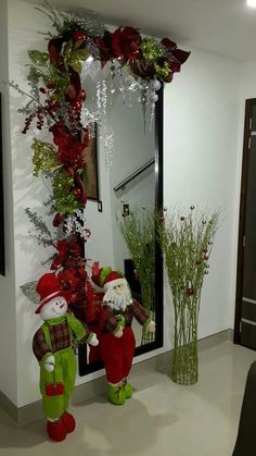 two green and red christmas decorations in front of a mirror with flowers on the wall