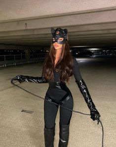 a woman in black catsuits holding a whip with her hands and wearing cat ears