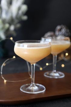 two glasses filled with drinks sitting on top of a wooden tray next to each other