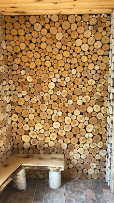 a wooden bench sitting in front of a wall made out of tree trunks and logs