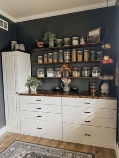 a kitchen with white cabinets and shelves filled with jars, containers and other items on top of them