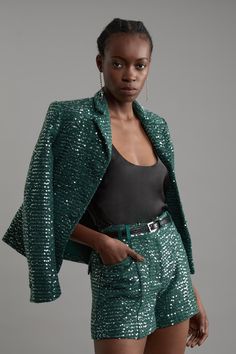 a woman in green sequins is posing for the camera with her hand on her hip