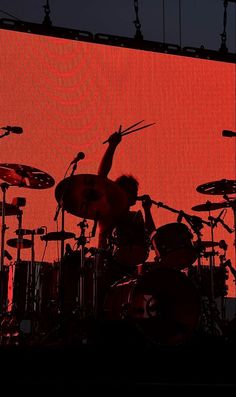 the drummer is playing drums on stage in front of an orange screen with his hands up