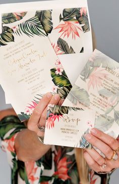 a woman holding up some cards with flowers on them and the words tropical wedding written in gold