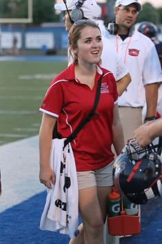 a woman in red shirt and white shorts walking on the field with helmeted headgear