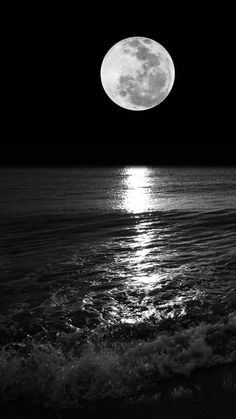 the full moon is shining over the ocean and waves on the beach at night time