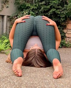 a woman is doing yoga outside in front of some plants and bushes, with her hands on her head