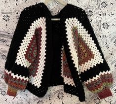 a crocheted jacket is hanging on a white tablecloth with black and red accents