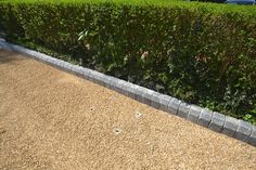 a hedge next to a graveled area in front of a car parked on the street