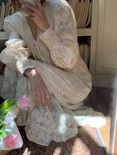 a woman sitting on the floor looking at her cell phone while wearing a white dress