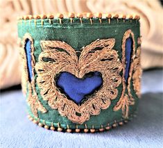 a close up of a green and gold cuff with a blue heart on it's side