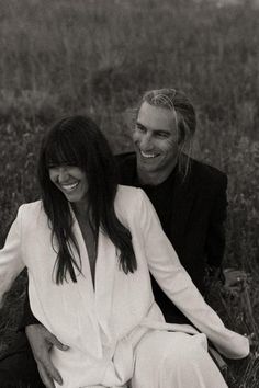 black and white photograph of two people sitting on the ground in tall grass smiling at each other