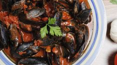 a bowl filled with mussels covered in sauce and garnished with parsley