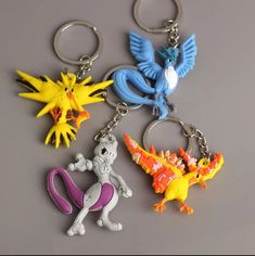 three key chains with different colored pokemons on them and one has a blue, yellow, red, and orange bird