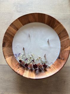 a wooden bowl filled with flowers on top of a white tablecloth covered floor next to a candle