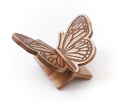 a wooden butterfly figurine sitting on top of a piece of wood with its wings open