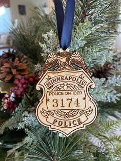 a police badge ornament hanging from a christmas tree in front of pine cones