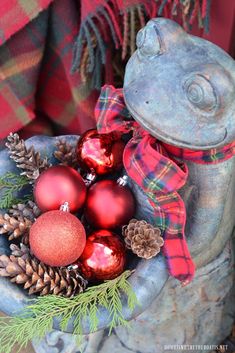 a metal bowl filled with ornaments and pine cones on top of a wooden table next to a plaid blanket