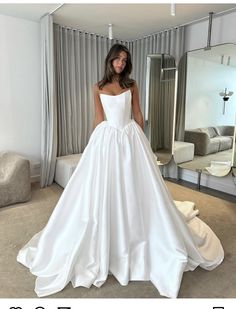 a woman standing in front of a mirror wearing a white wedding dress