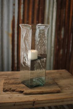 a glass vase sitting on top of a wooden table with a lit candle in it