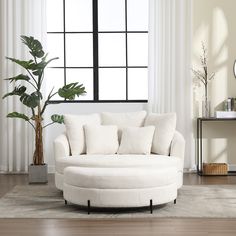 a living room with a large white couch and round ottoman in front of a window