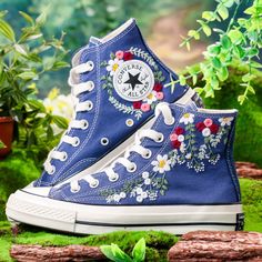 a pair of blue sneakers with flowers painted on them are sitting in the middle of moss