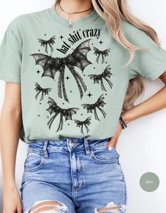 Unleash your wild side with our Batty Bows Crazy Tee! This Halloween-themed shirt features adorable bat-shaped bows, adding a quirky and playful twist to your spooky season wardrobe. Crafted from soft, breathable fabric, it's perfect for all-day comfort, whether you're trick-or-treating or attending a Halloween party. Make a bold statement and show off your unique style with this fun and festive tee. Embrace the Halloween spirit and get ready to turn heads with your batty, bow-tastic look! Perfect for bat lovers and Halloween enthusiasts alike. Spooky Cotton Top With Cat Design, Bat T Shirt, Fitted Cotton Halloween T-shirt, Bat Shirt, Spooky Cotton T-shirt With Cat Print, Spirit Halloween, Chambray, Halloween Themes, Art Pictures