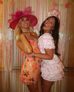 two beautiful young women standing next to each other in front of a wall with flowers