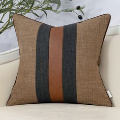 a brown and black striped pillow sitting on top of a white couch next to a potted plant