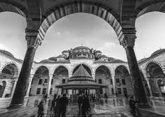 black and white photograph of people walking in front of an ornate building with arches on both sides