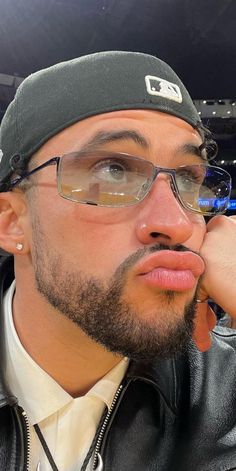 a man wearing glasses and a leather jacket at a baseball game with his hand on his chin