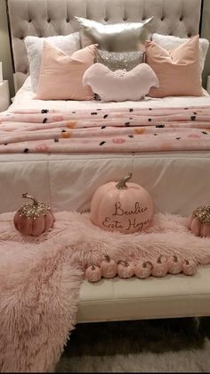 a white bed topped with pink pillows next to two pumpkins on top of a bench