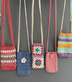 four crocheted purses hanging from hooks on a gray wall, one with a flower in the center