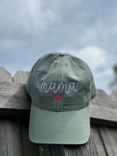 a green hat with the word mama written on it sitting on top of a wooden fence