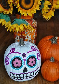 two pumpkins with sunflowers in the background and one painted as a skull