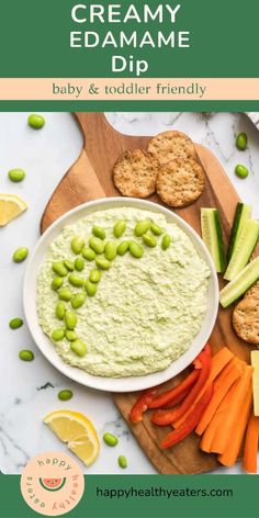 a bowl of creamy edamame dip surrounded by vegetables and crackers