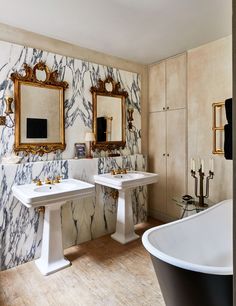 two white sinks sitting next to each other in a bathroom with gold framed mirrors on the wall