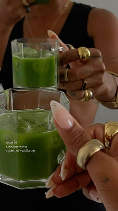 two women holding glasses with green liquid in them and gold rings on their fingers as they look at each other