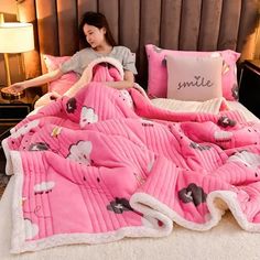 a woman sitting on a bed covered in pink sheets and blankets with cartoon animals all over them