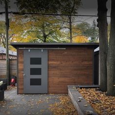 a small wooden shed in the middle of a park with leaves on the ground and trees surrounding it