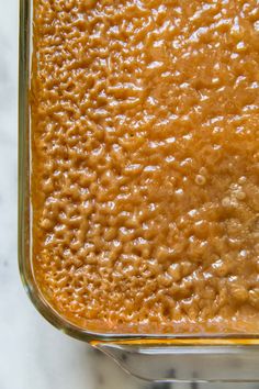 a glass dish filled with brown sauce on top of a white marble countertop next to a knife