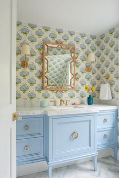 a bathroom with blue cabinets and wallpaper on the walls, along with a gold framed mirror