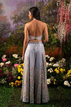 Element of fun and ethereal crafted in one ensemble. Sofia co-ord set consists of a halter neck top paired up with wide-legged pants accentuated with tassel drops. The ice-blue hue of the ensemble makes one look surreal and elegant while at the same time, the silhouette defines your bubbliness. Halter neck blouse embroidered with daisy motifs highlighted with sequins and flowers. Wide-legged pants with attached crisscross studded straps at the waistline crafted out of blingy sequined fabric high Lehenga Pants Designs, Indian Outfits Pants, Blue Palazzo Set For Spring Party, Summer Embellished Pant Set For Party, Halter Neck Suits Indian, Party Sets With Back Tassel Tie-up, Spring Party Sets With Tassels, Summer Wedding Wide Leg Palazzo Set, Summer Palazzo Set With Tassels