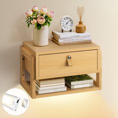 a nightstand with flowers and books on it next to a wall mounted clock, lamp and phone charger